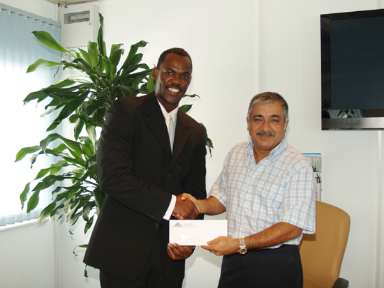 GEBE managing director, William Brooks, presents the donation check to University of St. Martin board member, Danny Ramchandani. usmdonation